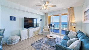 A living room with a TV, sofa, and a view of the ocean. - Emerald Gem - Gulf Coast View! (Panama City Beach)