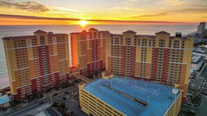 A high-rise hotel with multiple balconies, a parking garage, and a view of the sunset over the ocean. - Emerald Gem - Gulf Coast View! (Panama City Beach)