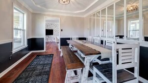 Uma sala de jantar ampla com bancos e mesas de madeira branca, parede estampada e luminária geométrica no teto.