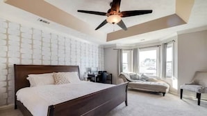 Quarto com cama de madeira, ventilador de teto, sofá e uma cadeira.