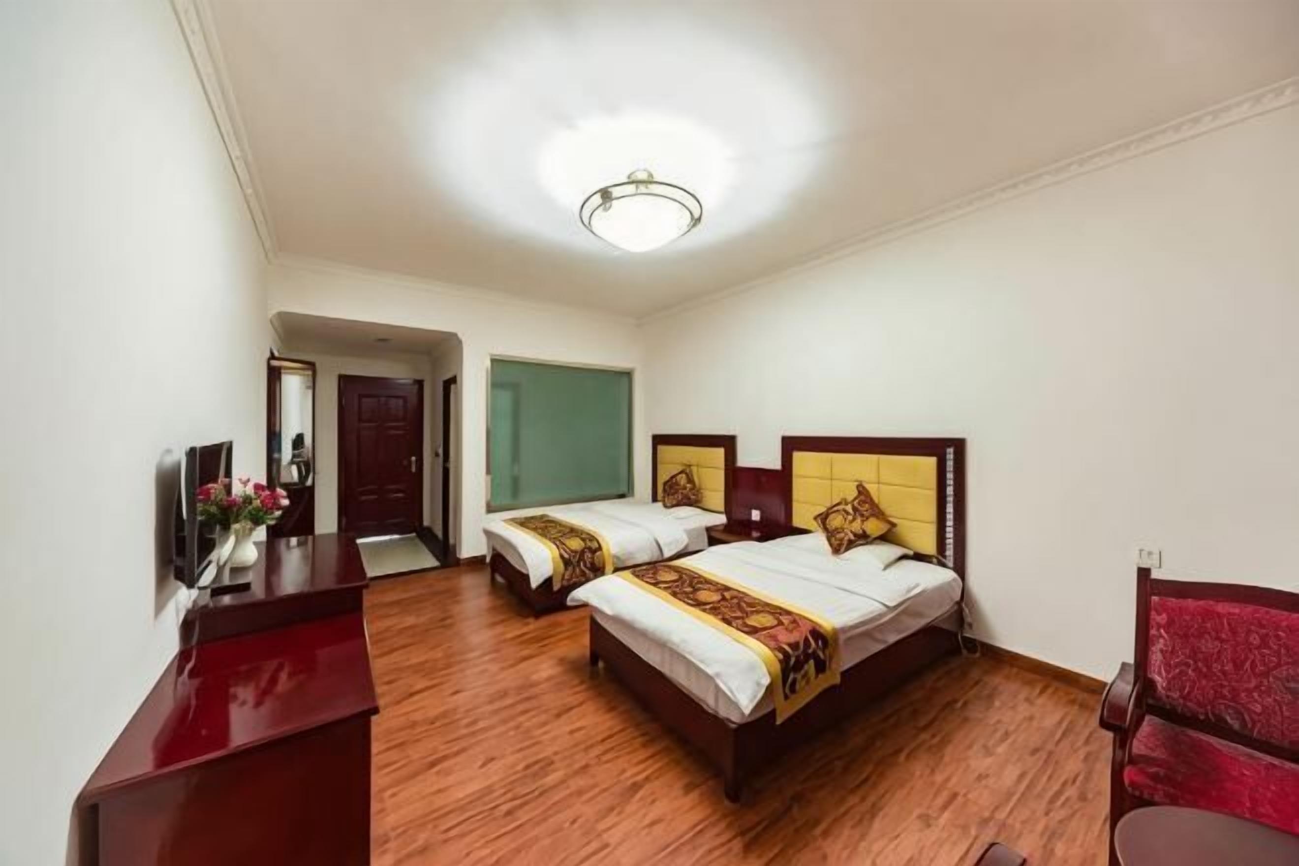 A hotel room with two beds, a desk, a chair, and a television.