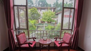 A room with two wooden chairs and a small table, large windows with a view of a building and greenery outside. - Jieya Hotel (Emeishan City)