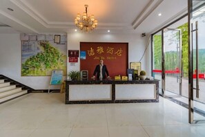 A hotel reception desk with a large sign, a chandelier, and a staircase leading to the upper floor. - Jieya Hotel (Emeishan City)