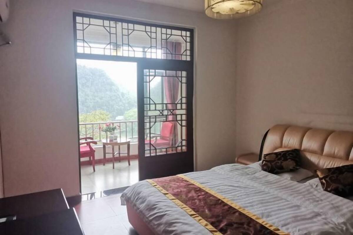 Une chambre avec un lit, un balcon avec des chaises et une vue sur la verdure.