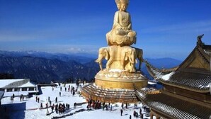 A large golden statue of a seated figure with a backdrop of mountains and traditional architecture. - Jieya Hotel (Emeishan City)