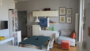 A modern living room with a dining table, chairs, a sofa, a bookshelf, and a TV. - "Nea Parthenope" apartment. (Napoli)