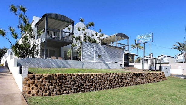 A modern two-story house with a balcony, a stone retaining wall, and a sign indicating 'SING CASTLES on the beach NO VACANCY'. - Sandcastles Unit 8 - 2 bedroom Ocean Front Unit (Bargara)