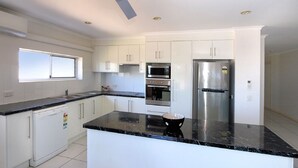 A modern kitchen with white cabinets, a black countertop, stainless steel appliances, and a window providing natural light. - Sandcastles Unit 8 - 2 bedroom Ocean Front Unit (Bargara)