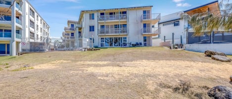 A multi-story residential building with balconies, a fenced yard, and a clear sky.
