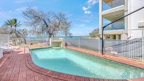 A swimming pool with a view of the sea, surrounded by a fence, and a building with a balcony. - Shoreline Apartments - Unit 10 (Bargara)