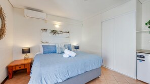 A bedroom with a bed, bedside tables, a wall-mounted air conditioner, and a white wardrobe. - Shoreline Apartments - Unit 10 (Bargara)