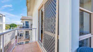 A balcony with a white railing, a view of the street, and a building with a tiled roof. - Shoreline Apartments - Unit 10 (Bargara)