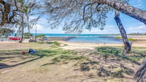 A beach with a clear view of the ocean, a red car parked on the sand, and a person sitting on the grass. - Shoreline Apartments - Unit 10 (Bargara)