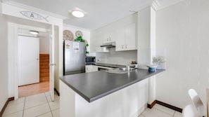 A modern kitchen with white cabinetry, a stainless steel refrigerator, a microwave, and a large island with a sink. - Shoreline Apartments - Unit 10 (Bargara)