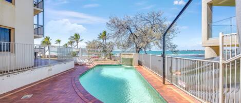 A swimming pool with a clear view of the ocean, surrounded by a white fence, and a brick pathway leading to the pool.