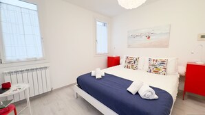 A hotel room with a bed, a desk, a chair, a red nightstand, and a painting on the wall. - Maison De La Brodeuse by Ca-sa Check (Chioggia)