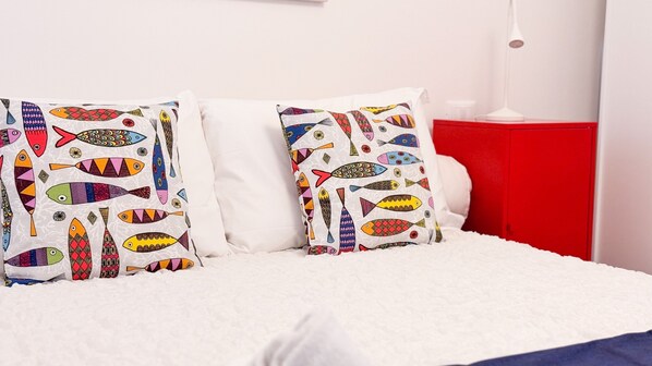 A bed with white bedding and two pillows featuring colorful fish patterns.