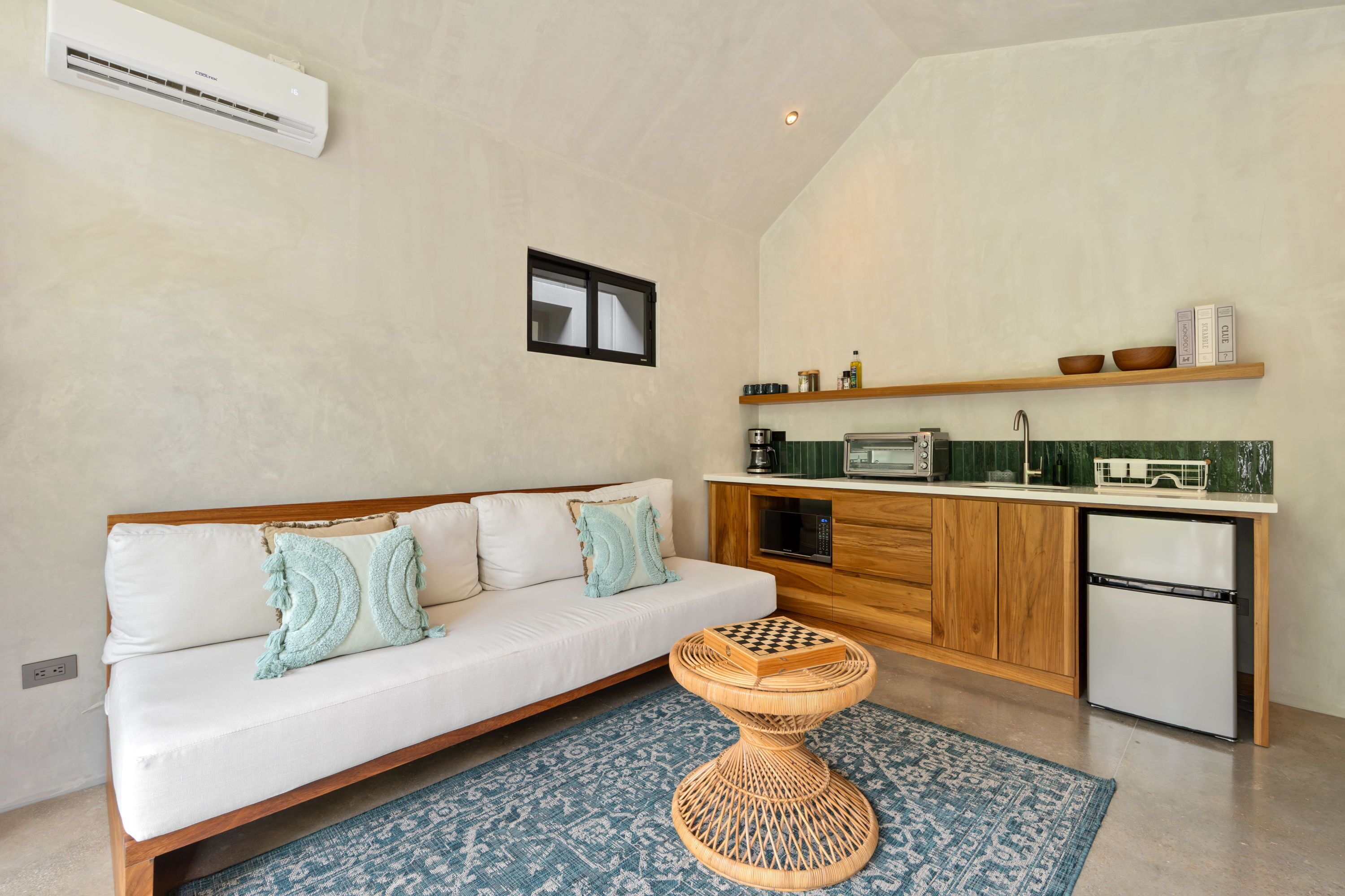A compact living space with a sofa, a small round table, a kitchenette, and a window.
