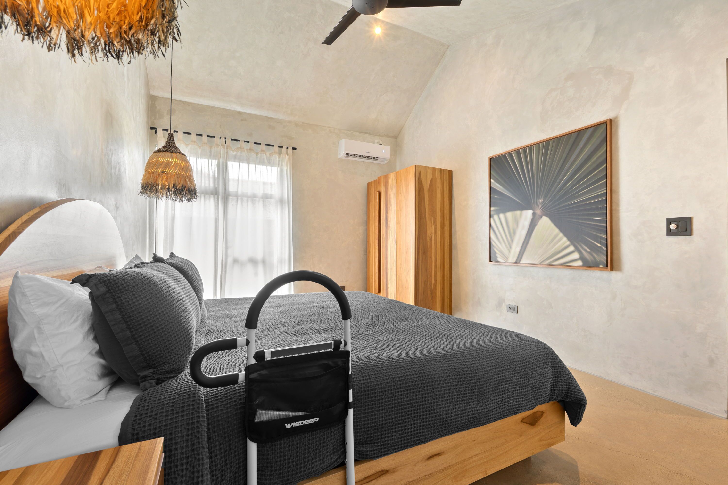 Ein modernes Schlafzimmer mit Bett, Deckenventilator, Wandklimaanlage und einem großen abstrakten Gemälde.