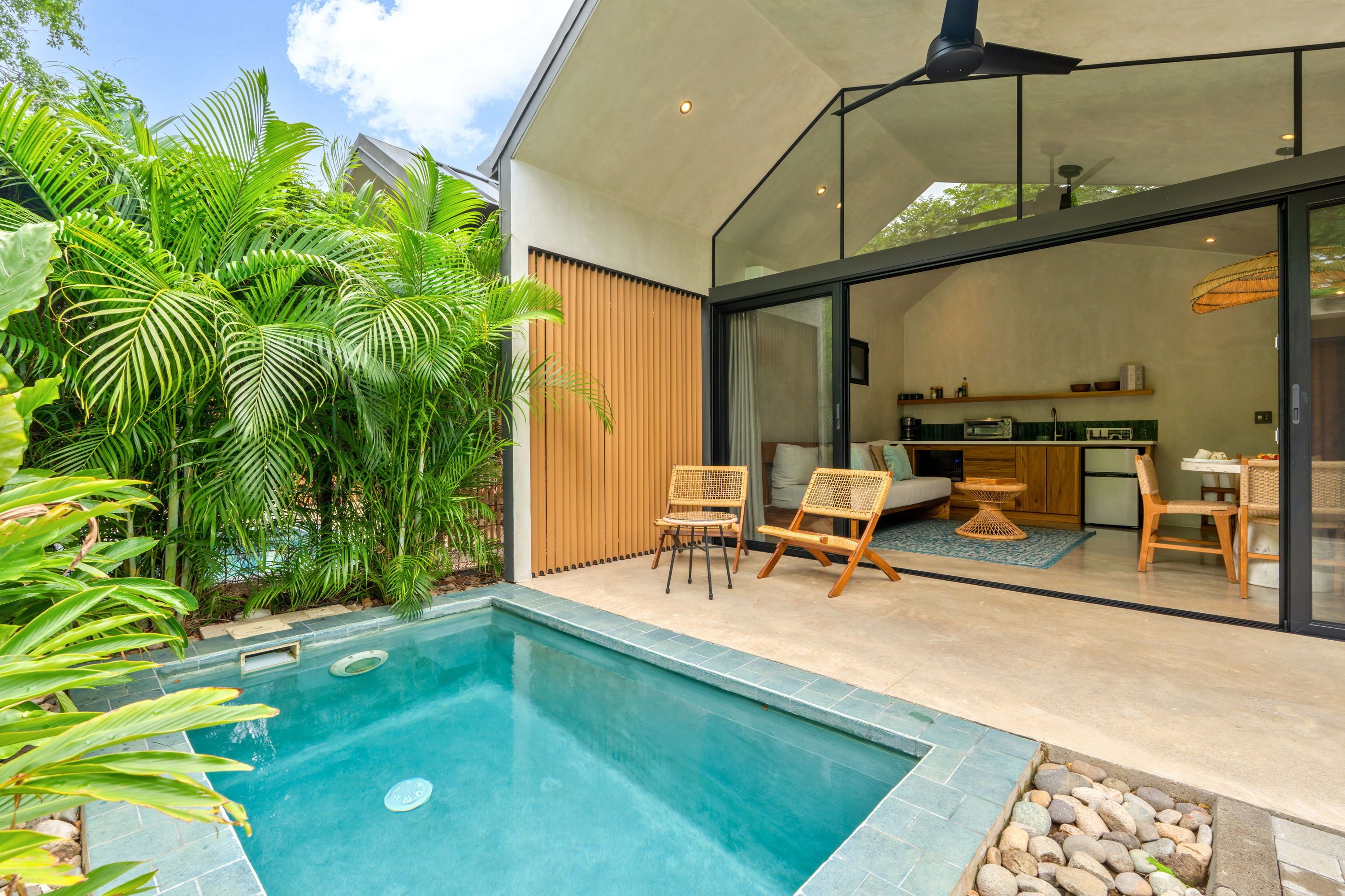 Une maison moderne dotée d’une piscine, d’un espace salon extérieur et d’une cuisine visible à travers des portes vitrées.