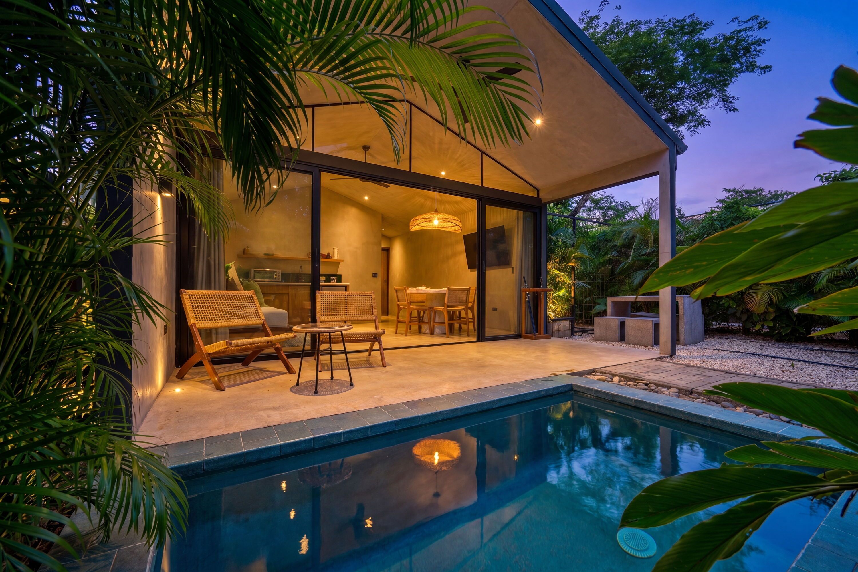 A modern house with a swimming pool, outdoor seating, and a kitchen visible through glass doors.