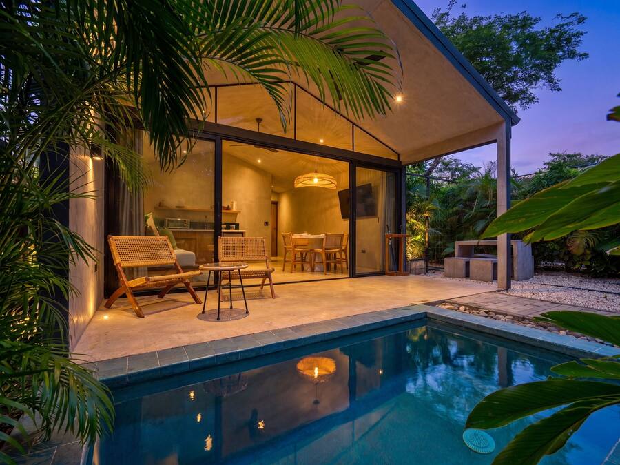 A modern house with a swimming pool, outdoor seating, and a kitchen visible through glass doors.