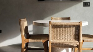 A modern dining area with a round table, two wicker chairs, a woven pendant light, and a flat-screen TV mounted on the wall. - Selvatico Tamarindo Villas (Tamarindo)