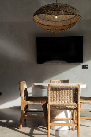 Een moderne eetruimte met een ronde tafel, twee rieten stoelen, een geweven hanglamp en een flatscreen televisie die aan de muur is bevestigd.