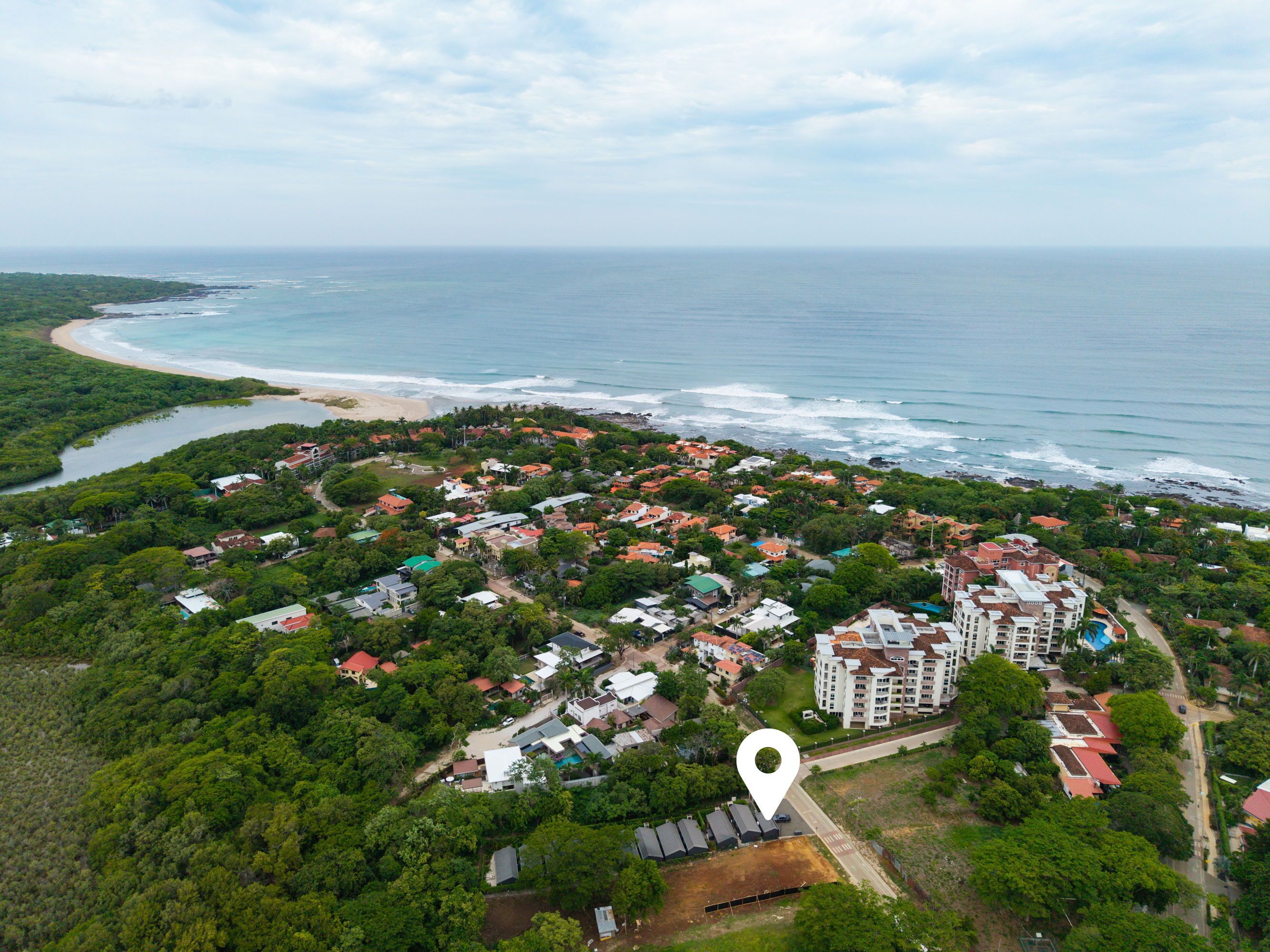 Vista aérea de una zona residencial costera con abundante vegetación, propiedades frente a la playa y un complejo de edificios grandes.