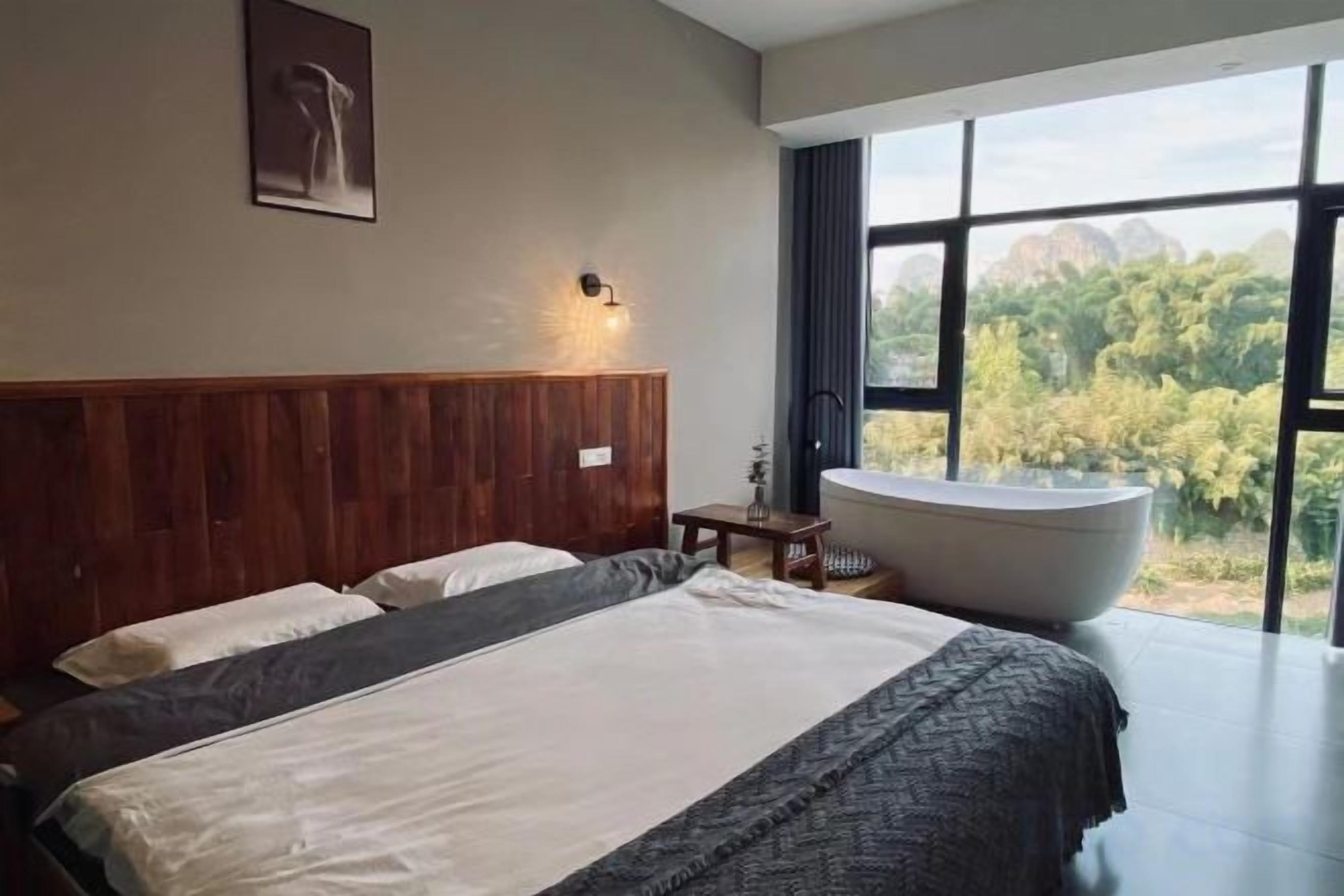 Une chambre moderne avec un grand lit, une baignoire et une vue sur la verdure grâce à de grandes fenêtres.