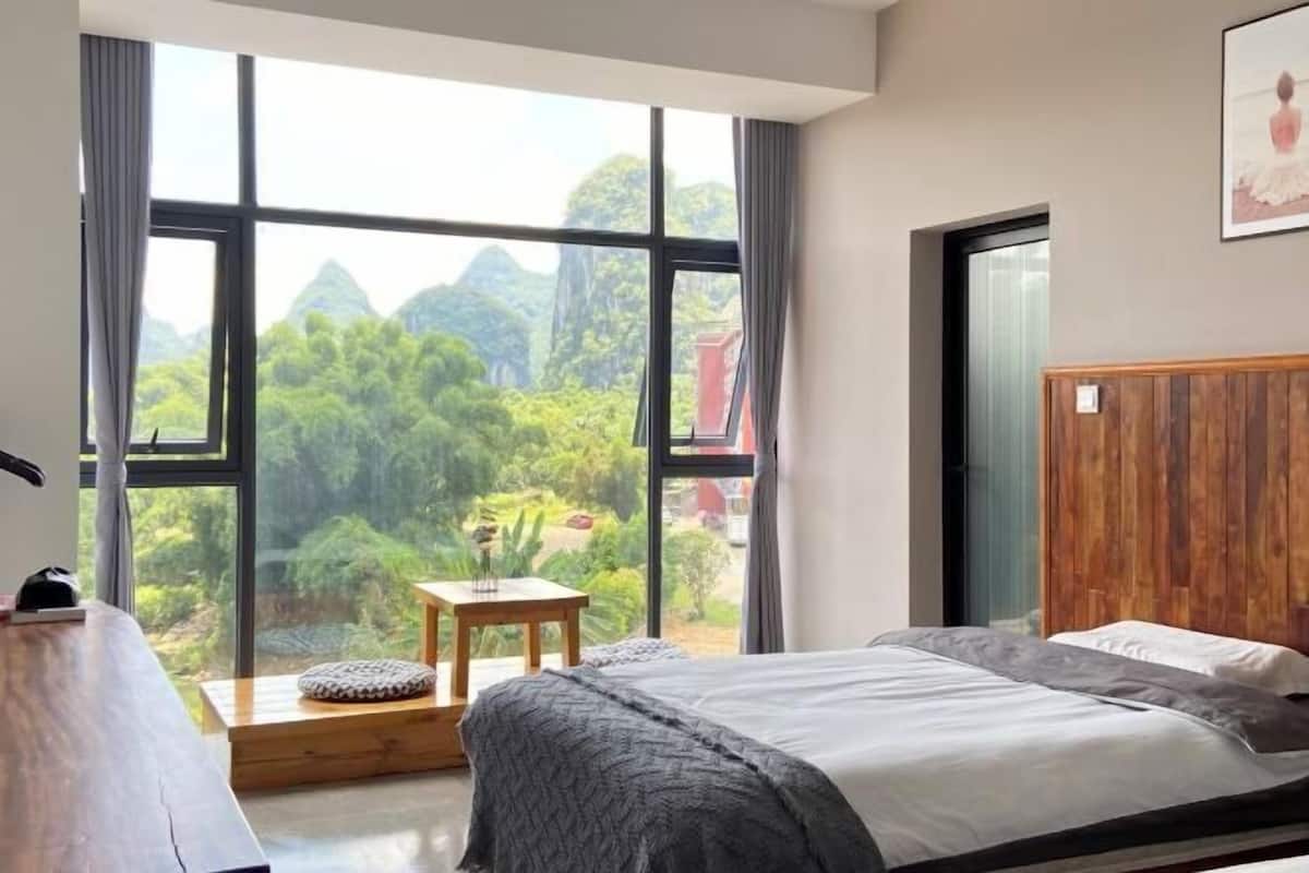 A bedroom with a large window, a wooden headboard, a bedside table, and a bed.