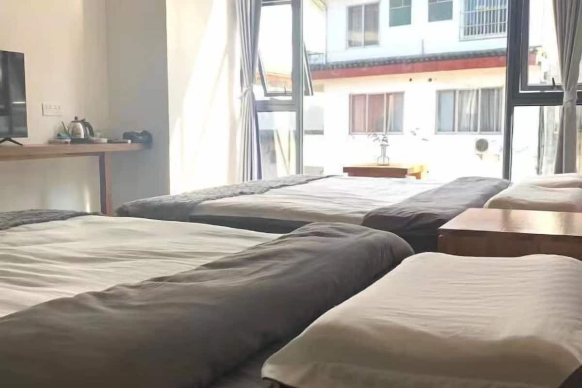 A hotel room with three beds, a desk with a computer, and a window with a view of a building.