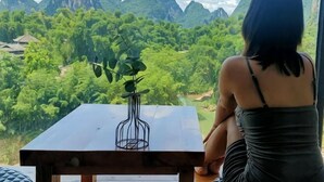 A person seated at a table with a view of a mountainous landscape. - Qiqi Xiaozhan (Yangshuo Impression Liusanjie Scenic Area Shop) (Yangshuo)