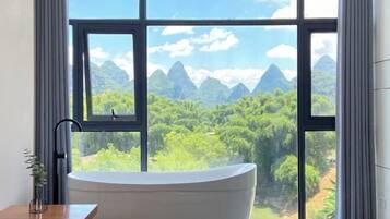 A modern bathroom with a freestanding bathtub, large windows, and a view of a mountainous landscape.