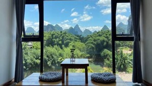 A room with a large window overlooking a mountainous landscape. - Qiqi Xiaozhan (Yangshuo Impression Liusanjie Scenic Area Shop) (Yangshuo)