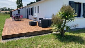 Una casa moderna con terraza de madera, mobiliario exterior y un pequeño jardín.