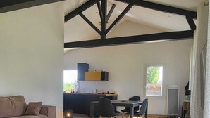 Un salón amplio con sofá, mesa baja y mesa de comedor con sillas. Se observa una cocina al fondo, con una ventana.