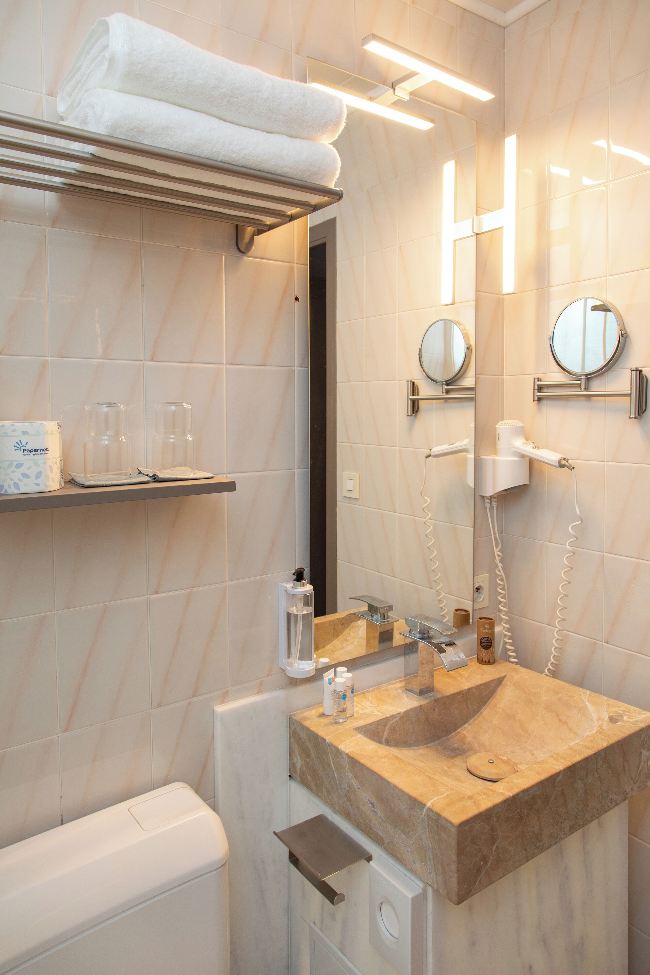 A modern bathroom with a marble sink, towel rack, and a hairdryer on the wall.