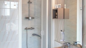 A modern bathroom with a marble sink, a glass shower enclosure, and a built-in shelf with toiletries.
