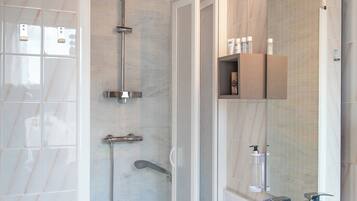Un baño moderno con un lavabo de mármol, cabina de ducha de vidrio y estante empotrado con artículos de aseo.