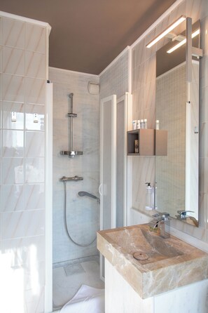 A modern bathroom with a marble sink, a glass shower enclosure, and a built-in shelf with toiletries.