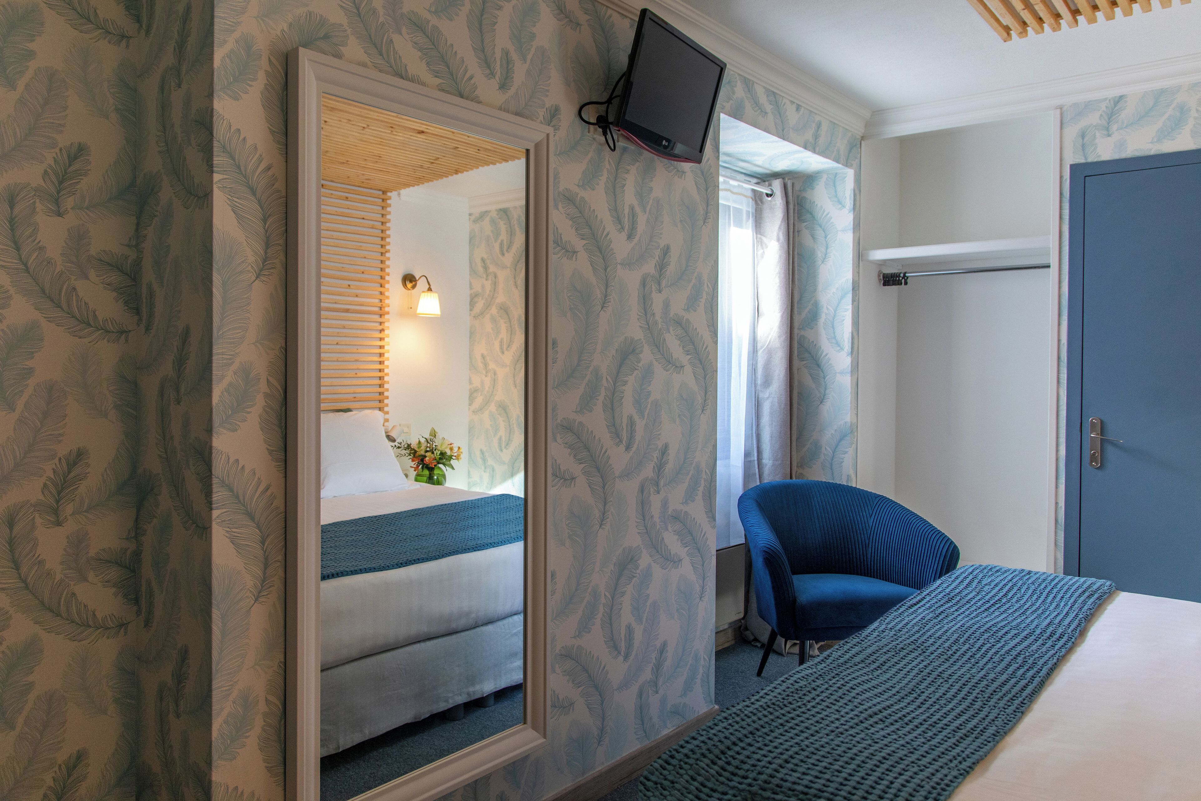 A hotel room with a bed, a chair, a television mounted on the wall, and a door.
