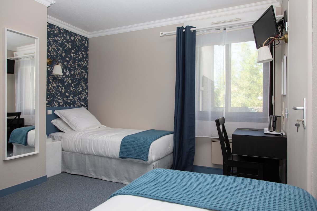 A bedroom with two beds, a desk, a chair, a TV, and a window with curtains.