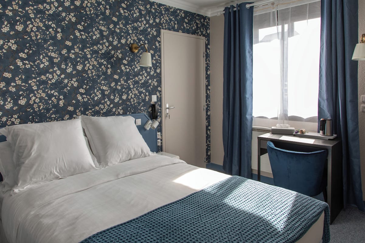 A hotel room with a bed, a desk, and a window with curtains.