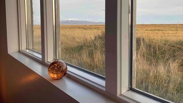 Una ventana con vistas a un campo cubierto de hierba y una cordillera lejana.