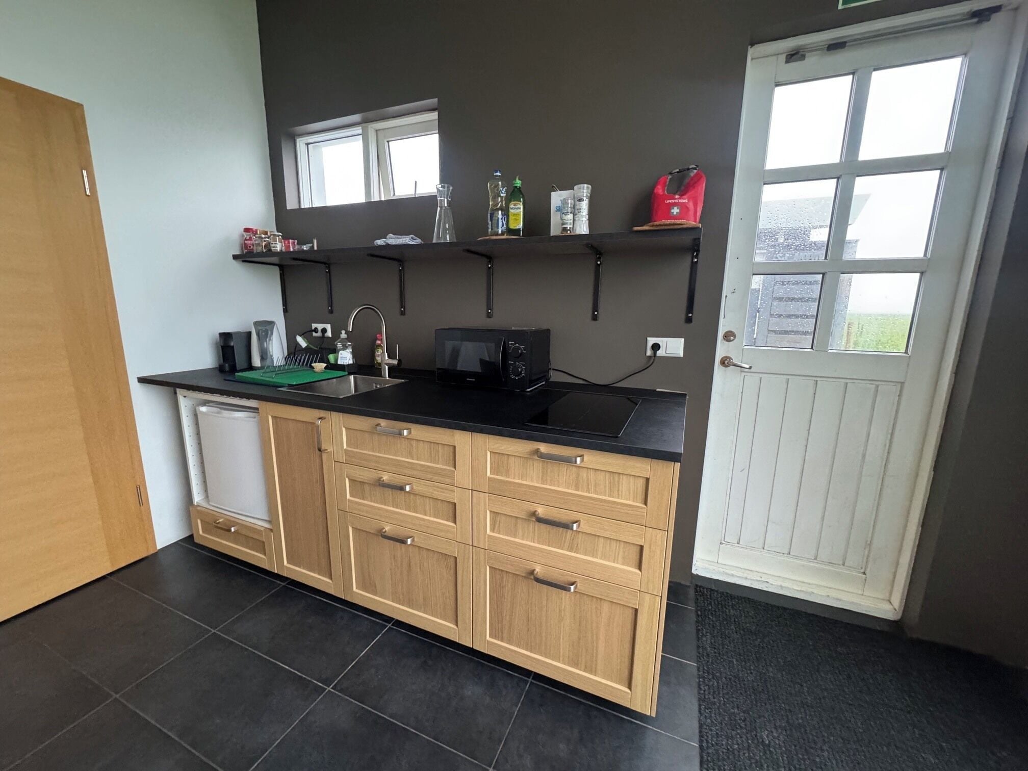 A compact kitchen with a black countertop, wooden cabinets, a built-in dishwasher, and a window above the sink.