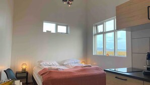 Un dormitorio con cama, mesita de noche, lámpara y vistas al exterior a través de una ventana.