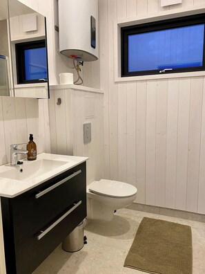 Un baño moderno con un lavamanos blanco, tocador negro, inodoro y ventana con vista azul.