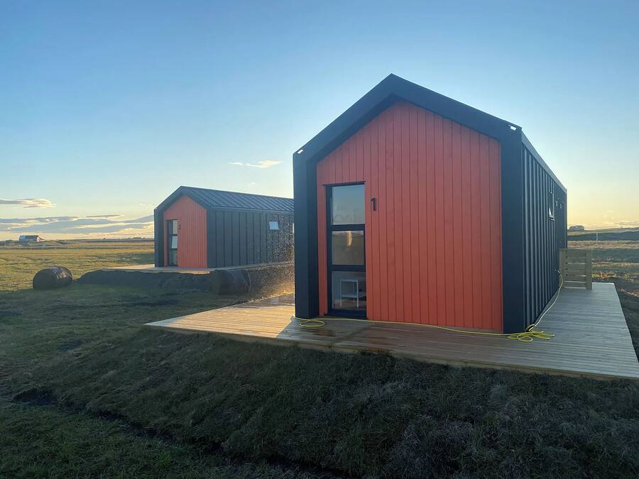 Two modern, red and black cabins with wooden decks, set in a grassy field with a clear sky.