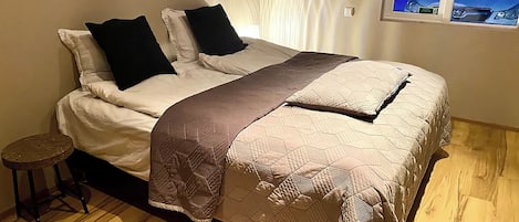 Una cama con cubrecolcha acolchado, dos almohadas negras y una manta marrón.